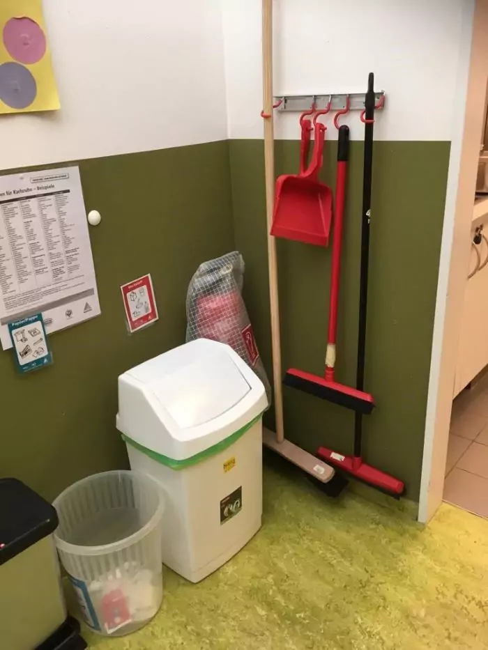Verschiedene Mülleimer, ein verpackter Feuerlöscher und an der Wand aufgehängte Besen in einer ordentlichen Ecke