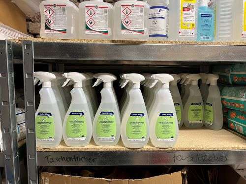 Putzmittelflaschen aufgereiht im Regal, darunter die Beschriftung 'Taschentücher, Feuchttücher'