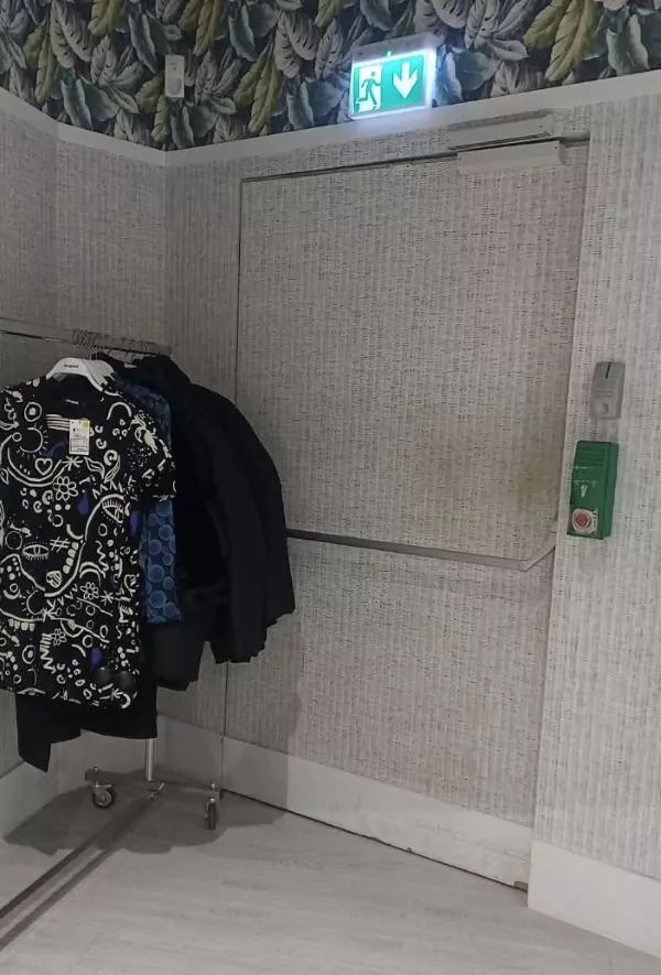 Ein verstellter Notausgang in einem Geschäft. Vor der Tür steht ein Kleiderständer